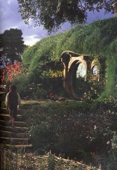 the hobbot house is surrounded by lush green plants and trees, with stairs leading up to it