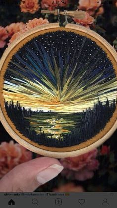 someone is holding up a small embroidery art piece with the sun setting in the background