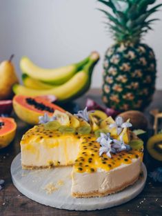 there is a cheesecake with fruit on the table next to bananas and pineapples