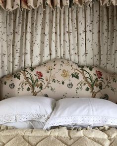 an upholstered bed with white pillows and floral wallpaper on the headboard