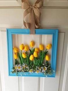 a blue frame with yellow tulips and daisies in it hanging on the wall