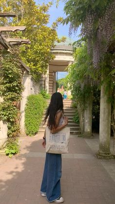 a woman is walking down the sidewalk carrying a bag with writing on it and trees in the background