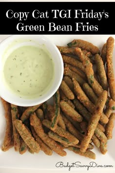 a white plate topped with fried green bean fries and a small bowl of dipping sauce