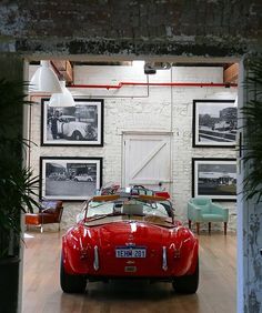 an old red sports car is parked in a room with framed pictures on the wall