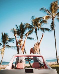 two women sitting in the back of a car with their arms up and palm trees behind them