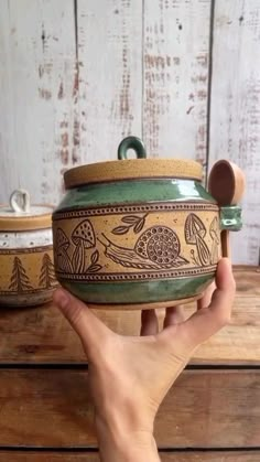 a hand holding a green and brown pot on top of a wooden table