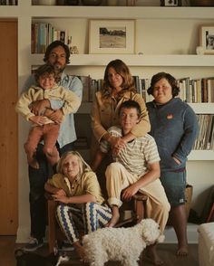 a family poses for a photo in front of bookshelves with a dog on the floor