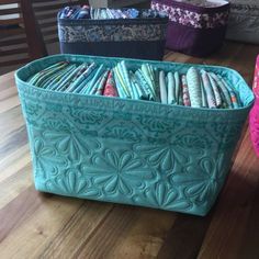 several fabric storage bins on a wooden floor with one filled with colorful fabrics and the other empty