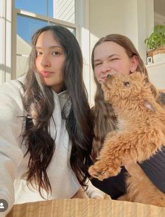 two women sitting at a table with a cat on their shoulders and one holding the cat up to her face