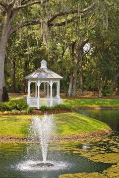 a white gazebo in the middle of a pond surrounded by trees and water lilies