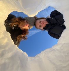 two people are standing in the middle of a heart shaped hole with snow on it