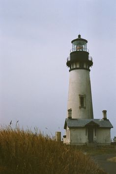 an old lighthouse sits on top of a grassy hill