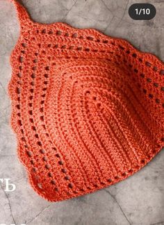 an orange crocheted hat laying on top of a stone floor next to a pair of scissors