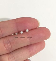 a person's hand holding a tiny silver nose ring with two balls on it