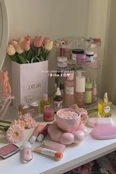 a white table topped with lots of pink flowers and cosmetics next to a vase filled with tulips