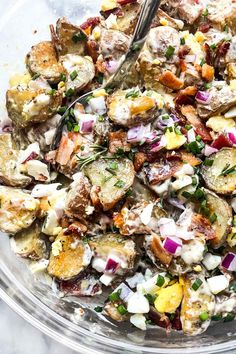 a glass bowl filled with potato salad on top of a marble countertop next to a metal fork