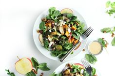 two plates filled with salad and dressing on top of a white table next to silverware