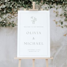 an easel with a sign that says welcome to our wedding on it and greenery in the background