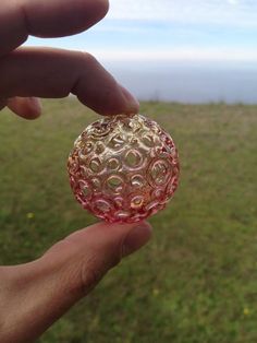 a hand holding a glass ball in the middle of a green field with grass and blue sky