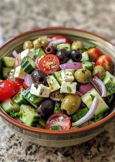 a bowl filled with olives, cucumbers and tomatoes on top of a table