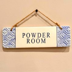 a sign hanging on the wall that says powder room with blue and white designs in it