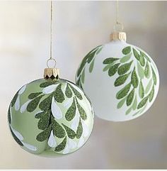 two green and white christmas ornaments hanging from strings with leaves painted on the top one ornament