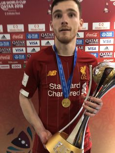 a man holding two trophies in front of a wall with other awards around his neck