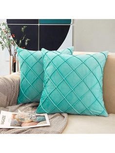 two pillows sitting on top of a couch in front of a vase with flowers and a magazine