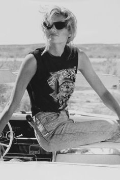 a woman sitting on the hood of a car with her legs crossed and wearing sunglasses