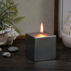 a lit candle sitting on top of a wooden table next to rocks and a potted plant