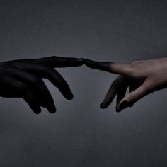 two hands reaching out towards each other with black paint on their fingertipss, against a gray background