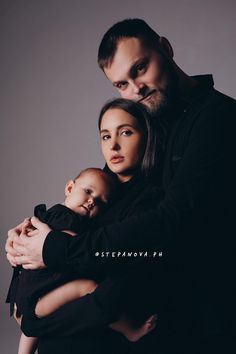 a man and woman holding a baby while posing for a photo in front of a gray background