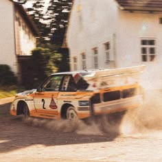 an orange and white car driving down a dirt road next to a tall white building