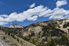 the mountains are covered with trees and clouds in the distance is a road that runs through them