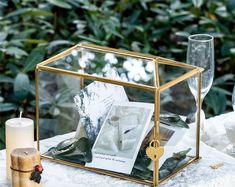 a glass box filled with pictures and two candles on top of a white table cloth