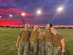 four women in camo pants are posing for a photo on the field at sunset