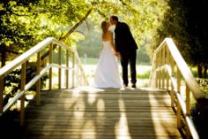 a bride and groom are standing on a wooden bridge in the sun with their arms around each other