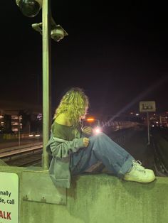 a woman sitting on the side of a train track next to a street light at night