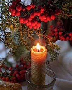 a lit candle sitting on top of a glass vase filled with berries and greenery