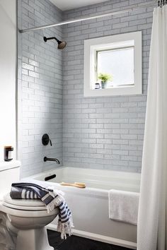 a white toilet sitting next to a bath tub under a window in a bathroom with black and white tile