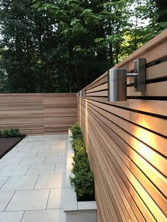 a wooden fence with lights on it next to some bushes and trees in the background