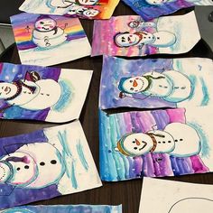 several snowmen are painted on paper with colored pencils and watercolor papers in front of them