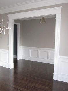 an empty living room with hard wood flooring and white trim on the walls, chandelier