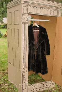 an open cardboard box with a coat hanging on the door and a dress in it