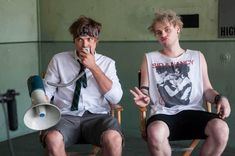 two young men sitting in chairs with one holding a megaphone and the other listening to something