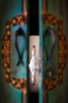 a woman in a white dress is walking through an open door with ornate designs on it