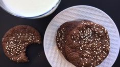 two cookies on a plate next to a glass of milk and a paper towel with sesame seeds