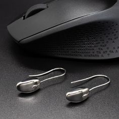 two pairs of silver earrings sitting next to a computer mouse on a black table top