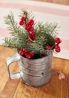 a christmas plant in a metal mug on a wooden table with red berries and pine needles