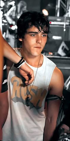 a young man in white tank top standing next to a woman wearing black bracelets